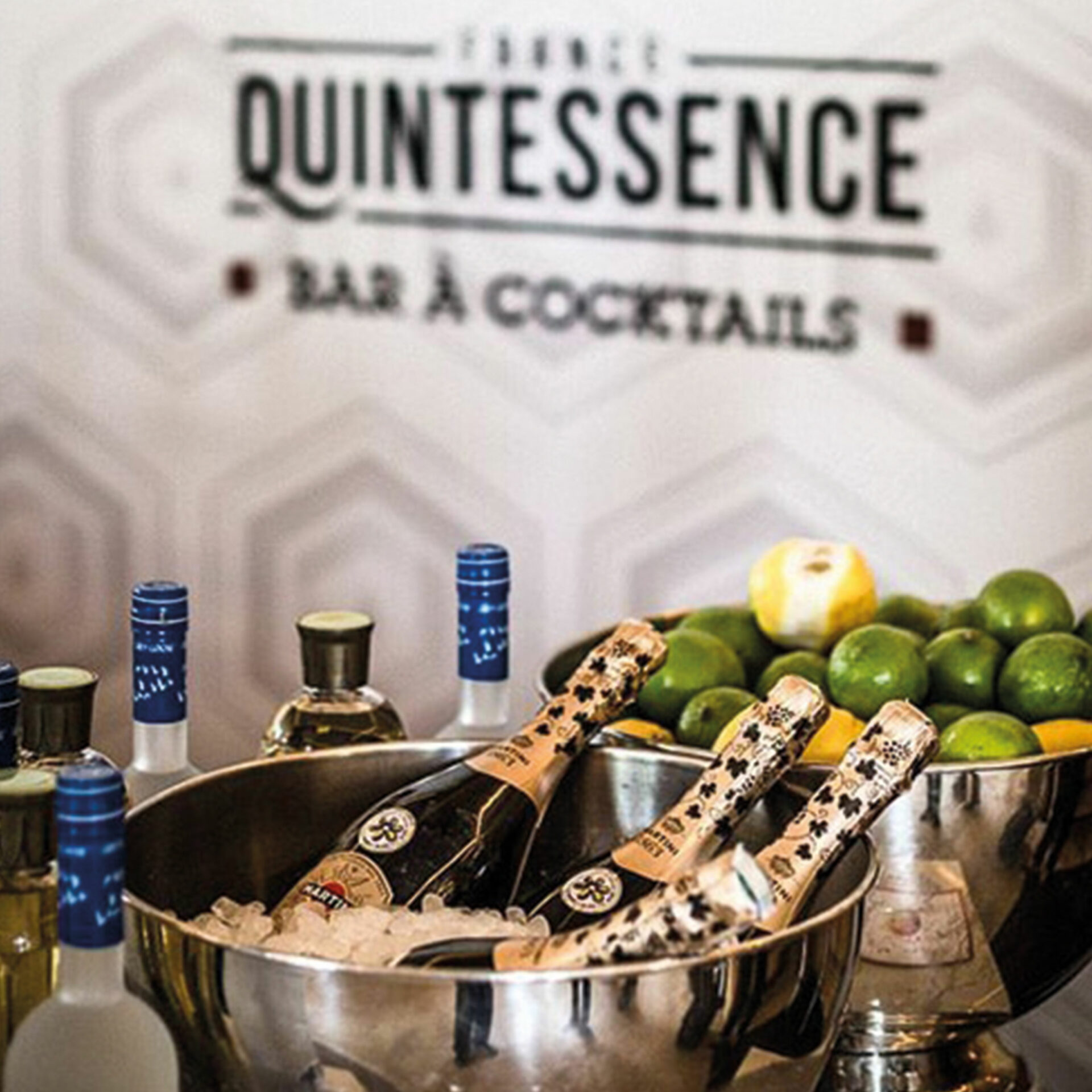 Bar à cocktail sur lequel sont disposées des bouteilles de champagne dans de la glace et des citrons jaunes et verts dans des culs de poule